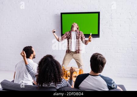 Aufgeregt Mann schreien und zeigt Sieg Geste in der Nähe lcd-tv Und multikulturelle Sportfans Stockfoto
