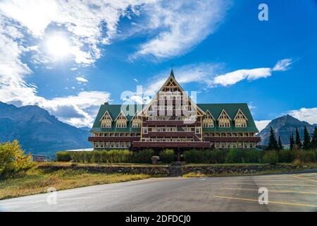 Prince of Wales Hotel im Herbst sonnigen Tag Morgen. Blauer Himmel, weiße Wolken über Bergen im Hintergrund. Wahrzeichen im Waterton Lakes National Park Stockfoto