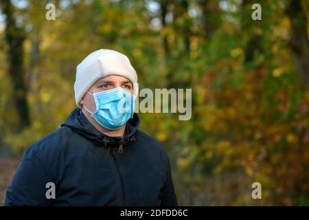 Ernst junger Mann trägt eine schützende Gesichtsmaske während der Coronavirus oder Covid-19 Pandemie Wandern durch Wald im Herbst in Ein Konzept der ne Stockfoto