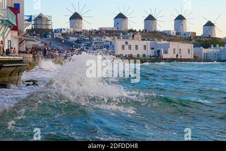 Mykonos, Griechenland - 10. September 2019: Zeitraffer, Touristen in der Nähe von 'Little Venice' bewundern den Sonnenuntergang. Im Hintergrund die Panorama-Windmühlen. Stockfoto