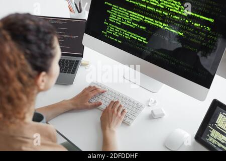 Rückansicht des Programmierers, der Computersystem aufrüstet, während er an sitzt Der Tisch vor dem Computermonitor Stockfoto