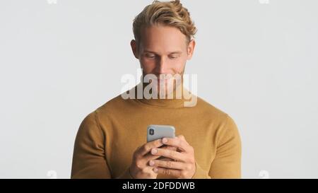 Schöner bärtiger Mann tragen Rollkragen Chat mit Freundin mit Smartphone isoliert auf weißem Hintergrund. Internetkommunikation Stockfoto