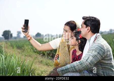 Glückliche indische Familie von Landwirt in landwirtschaftlichen Feld mit Telefon Stockfoto