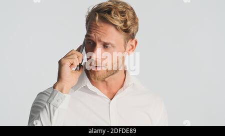 Gut aussehende bärtige Mann im Hemd ernsthaft im Gespräch mit Geschäftspartner auf dem Smartphone über weißem Hintergrund. Moderne Technik Stockfoto