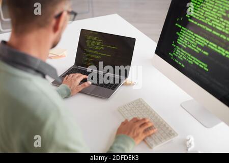 Rückansicht des reifen Programmierers, der am Tisch sitzt, der sich entwickelt Programm auf einem Desktop-Computer Stockfoto