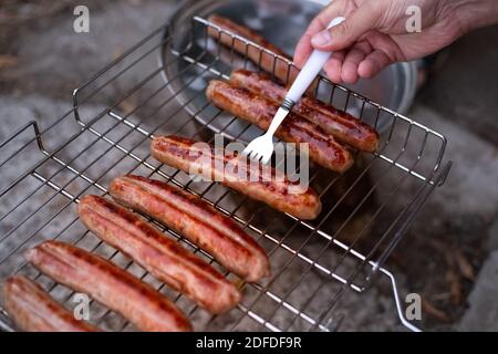 Gegrillte Fleischwürste. Der Mann dreht die fertigen Würstchen mit einer Gabel um. Oktoberfest. Stockfoto