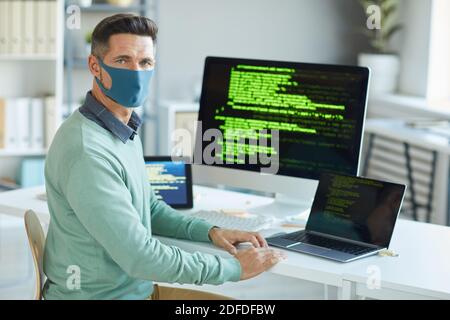 Porträt eines jungen Mannes in Schutzmaske Blick auf die Kamera Beim Schreiben von Codes im IT-Büro Stockfoto