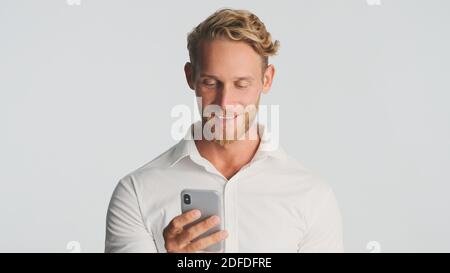 Schöner bärtiger Mann im Hemd selbstbewusst mit Smartphone für die Arbeit über weißem Hintergrund. Junger Geschäftsmann, der am Telefon arbeitet Stockfoto