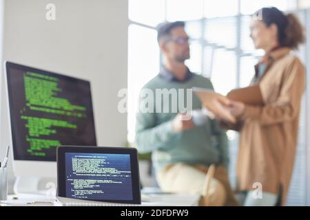 Bild von digitalen Tablet und Computer auf dem Tisch mit Menschen, die im Hintergrund im Büro miteinander sprechen Stockfoto