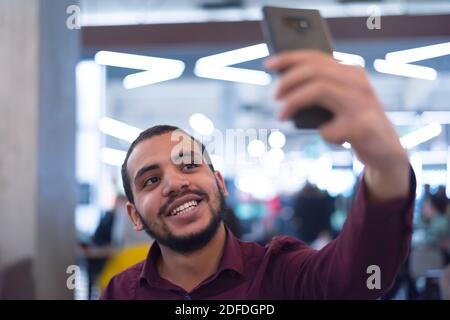 Lächelnder junger afrikanischer Mann mit Smartphone in einem modernen Café Stockfoto