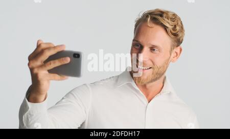 Schöner bärtiger Geschäftsmann im Hemd mit Videoanruf auf Smartphone über weißem Hintergrund. Modernes Technologiekonzept Stockfoto