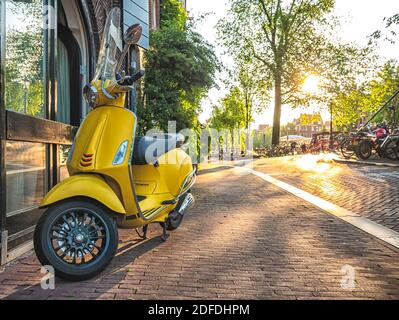 Gelber Oldtimer-Roller auf einem Bürgersteig geparkt. Scooter ist einer der beliebtesten Verkehrsmittel in Amsterdam Stockfoto