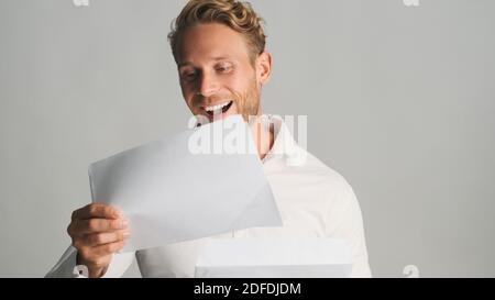 Junge fröhlich bärtigen Geschäftsmann in Hemd öffnen Umschlag mit Geschäft Dokumente und Freude an der Kamera isoliert auf weißem Hintergrund Stockfoto