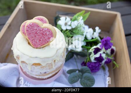 Ein cremiger Cupcake mit herzförmigen Plätzchen darauf und Blumen In einem Holztablett - Picknick-Idee Stockfoto