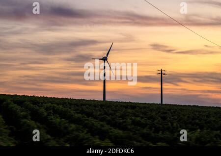 Windturbine und Hochspannungspylon auf dem Land Sonnenuntergang Stockfoto