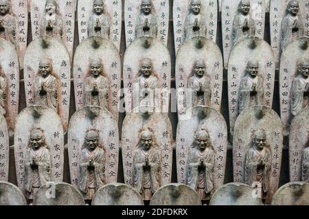 Horizontale frontale Nahaufnahme von Buddha-Steinstatuetten, die in Reihen im buddhistischen Tempel Daisho-in, Mt Mien, Miyajima, Japan, aufgestellt wurden Stockfoto