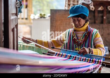 (201204) -- GONGSHAN, 4. Dezember 2020 (Xinhua) -- Kong Dangna webt einen Teppich im Dorf Kongdang der Gemeinde Dulongjiang, dem Autonomen Kreis Gongshan Dulong und Nu im Südwesten der Provinz Yunnan, 31. Oktober 2020. Die 78-jährige Kong Dangna aus der Dulong-Ethnie erlebte einst Jahre mit ungenügender Nahrung und Kleidung und lebte von Brandrost-Anbau. In jenen Tagen dachte sie, das beste Leben sei, Buchweizennudeln für jede Mahlzeit zu essen. Dank der Hilfe der lokalen Regierung zog Kongs Familie vom Berg in ein Gebiet in der Nähe des Dorfkomitees. Das neue Stockfoto