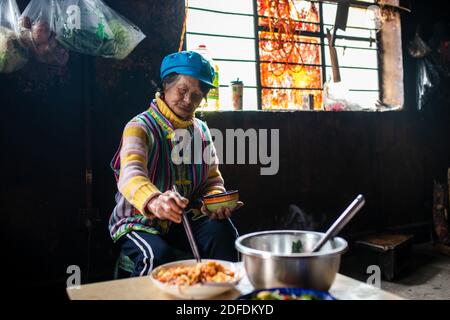 (201204) -- GONGSHAN, 4. Dezember 2020 (Xinhua) -- Kong Dangna isst Mittagessen im Dorf Kongdang der Gemeinde Dulongjiang, Gongshan Dulong und Autonomen Kreis Nu, südwestlich von Chinas Provinz Yunnan, 31. Oktober 2020. Die 78-jährige Kong Dangna aus der Dulong-Ethnie erlebte einst Jahre mit ungenügender Nahrung und Kleidung und lebte von Brandrost-Anbau. In jenen Tagen dachte sie, das beste Leben sei, Buchweizennudeln für jede Mahlzeit zu essen. Dank der Hilfe der lokalen Regierung zog Kongs Familie vom Berg in ein Gebiet in der Nähe des Dorfkomitees. Die neu-BU Stockfoto