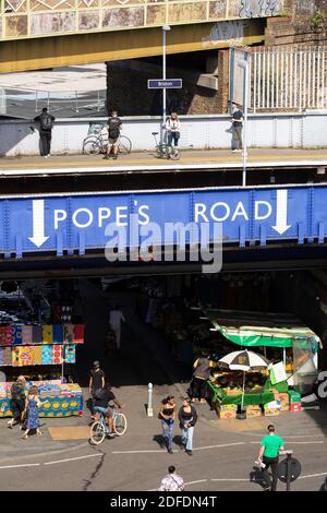 Fußgänger, die unter der Bahnüberführung auf der Pope's Road, Brixton, London, laufen Stockfoto