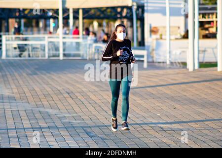 Huelva, Spanien - 3. Dezember 2020: Frau, die bei Sonnenuntergang an der Promenade von Huelva entlang läuft, mit schützenden oder medizinischen Gesichtsmasken während des Alarmzustandes und qu Stockfoto