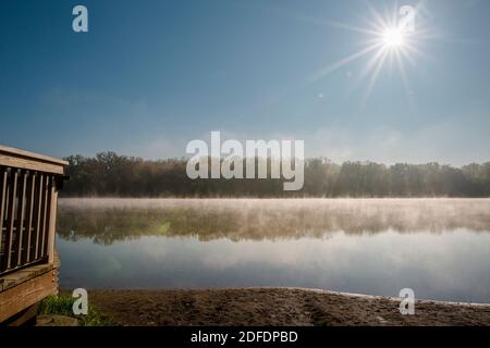 Die Sonne geht über einem nebligen See auf, in dem sich Bäume spiegeln Am frühen Morgen Stockfoto