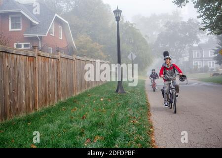 Ein Vater und ein Sohn fahren zusammen auf einem nebligen Baum gesäumt Straße Stockfoto