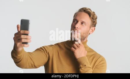Attraktive bärtige Mann im Rollkragendenken beim Gespräch mit Freunden auf Video-Chat isoliert auf weißem Hintergrund. Videoanruf Stockfoto