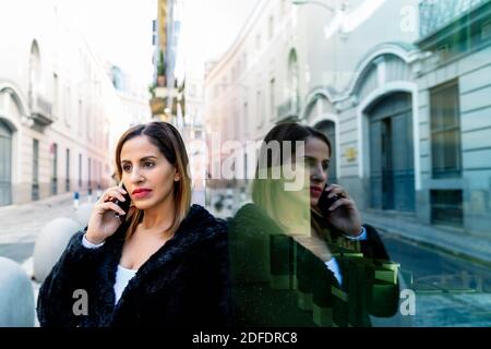 executive Frau in schwarzer Jacke im Gespräch auf ihrem Smartphone Stockfoto