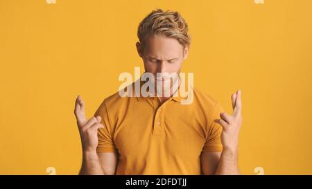 Attraktiver bärtiger Mann mit gekreuzten Fingern, der hoffentlich vor der Kamera betet Isoliert auf gelbem Hintergrund Stockfoto