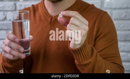Der Mensch nimmt Medizin mit einem Glas Wasser.Weiße Pille Eine junge männliche Hand Stockfoto