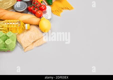 Flache Lay-Komposition mit Lebensmittelspenden auf grauem Hintergrund mit Copyspace - Pasta, frisches Gemüse, Konserven, Baguette, Speiseöl. Essen Stockfoto