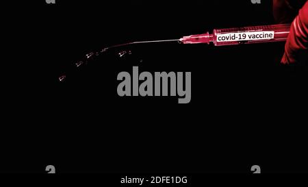 Spritze mit dem Text covid-19 Impfstoff, rote Spritze, Tropfen aus einer Nadel, auf schwarzem Hintergrund, Nahaufnahme. Stockfoto