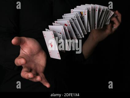 Mann macht Zaubertrick mit Spielkarte auf schwarzem Hintergrund. Stockfoto