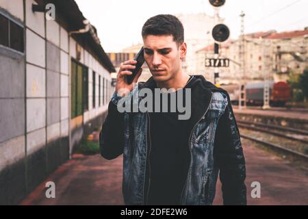 Junger Kaukasier, der am Bahnhof mit dem Handy spricht. Stockfoto