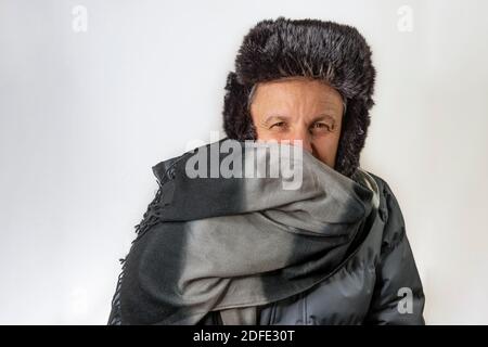 Der weiße Mann mittleren Alters, der vollständig mit Jacke, Wollschal und Pelzhut bedeckt ist, schützt sich vor Kälte und Wind Stockfoto