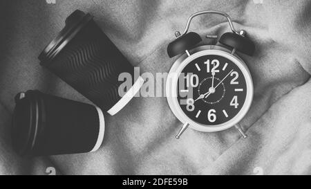 Retro-Uhr mit Wecker und mit Kaffee, Cappuccino, schwarz gerösteten Kaffee in Plastikgläsern, Draufsicht, schwarz-weiß-Bild. Stockfoto