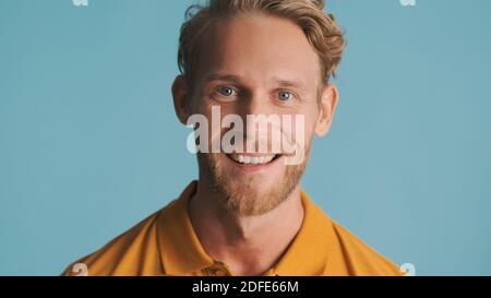 Porträt eines jungen bärtigen lächelnden Mannes, der aufgeregt auf isoliert schaut Blauer Hintergrund Stockfoto