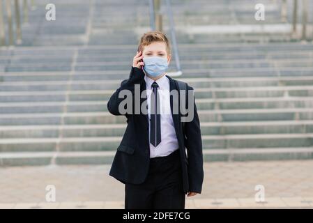 Schuljunge geht aus der Schule tragen Schutzmaske in der Stadt Stockfoto