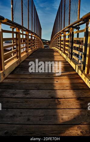 Perspektive einer Brücke mit Fokus auf den Holzboden Und Metallzaun bei Sonnenuntergang Stockfoto