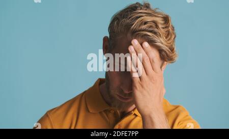 Junger bärtiger Mann sieht müde posiert vor der Kamera über bunten Hintergrund. Verärgerter Mann Stockfoto