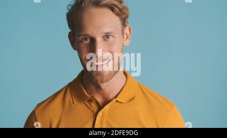 Attraktiver bärtiger Mann, der selbstbewusst in die Kamera schaut und isoliert auf blauem Hintergrund lächelt. Gesichtsausdruck Stockfoto