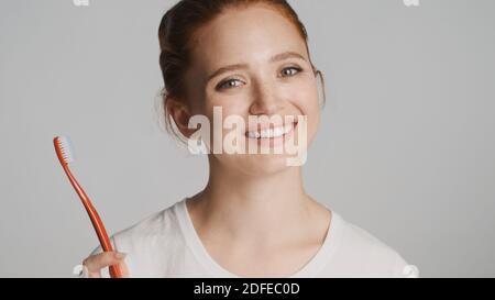 Schöne rothaarige Mädchen glücklich posiert mit Zahnbürste und lächelt an Kamera auf weißem Hintergrund Stockfoto