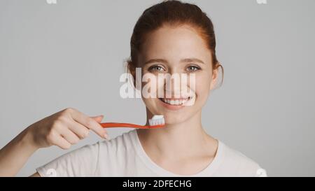 Schöne rothaarige Mädchen mit Zahnbürste glücklich suchen in der Kamera und Lächelnd isoliert Stockfoto