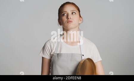 Attraktive Kellnerin in Schürze mit Tablett nachdenklich Blick weg über Weißer Hintergrund Stockfoto