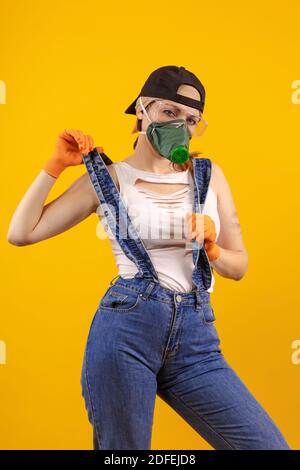 Baumeister Mädchen in Atemmaske in Denim Overalls und ein Schwarze Kappe posiert auf einem gelben Hintergrund Stockfoto