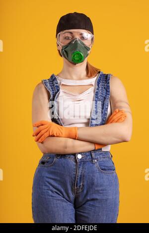 Baumeister Mädchen in Atemmaske in Denim Overalls und ein Schwarze Kappe posiert auf einem gelben Hintergrund Stockfoto