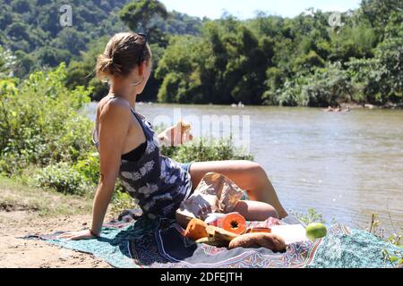 Eine Frau genießt ihr Picknick, während sie den Fluss betrachtet. Stockfoto