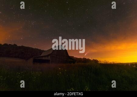 Eine alte Scheune sitzt in einer Weide in Jackson County, Indiana mit einem teilweise bewölkten Himmel über. Komet NEOWISE ist am Horizont. Stockfoto