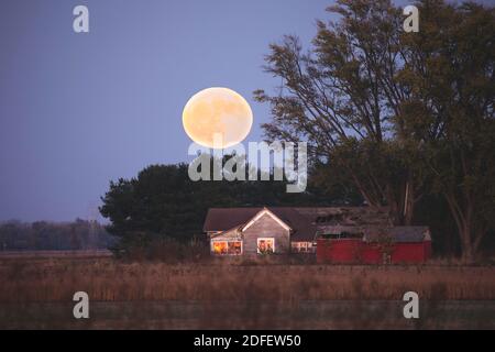 Ein verlassenes Haus mit einem großen Vollmond, der an einem Herbstabend in Jackson County, Indiana, darüber aufgeht. Stockfoto