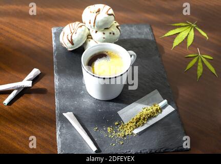 Perfektes Frühstück: Tablett mit Marihuanagelenken, frischem Kaffee und Schokoladendonuts auf Holztisch. Stockfoto